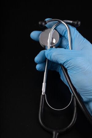 A metal stethoscope in a hand in a medical glove. Medical accessories in the hospital. Dark background.の写真素材