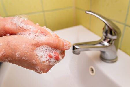 Washing hands with soap in the home bathroom. Soap skin on hands. Light background.