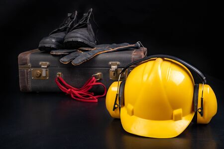 Protective helmet, suitcase and work shoes. Workwear for the production worker. Dark background.