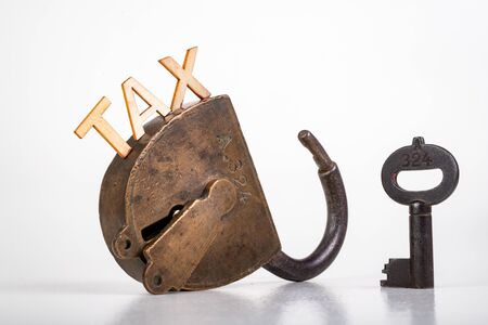 TAX inscription made of wooden letters. Old antique padlock and key. Light background.