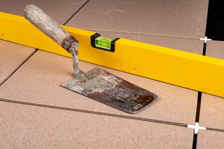 Laying gres tiles on warehouse spaces. Old spirit level and trowel for laying mortar. Dark...