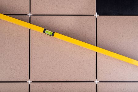 Laying gres tiles on warehouse spaces. Old spirit level to hold the floor level. Dark background.