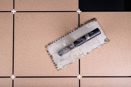 Laying gres tiles on warehouse spaces. Old trowel for laying mortar. Dark background.の写真素材
