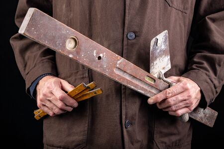 Bricklayer with a trowel and a spirit level in his hand. Worker in a construction site with tools. Dark background.の写真素材