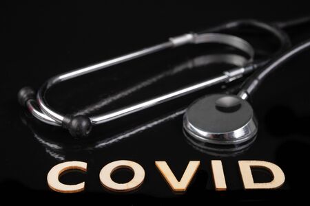 The inscription 'covid' made of wooden letters and a stethoscope. Virus name and medical accessories. Dark background.の写真素材