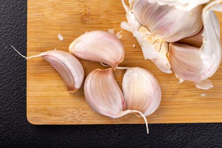 Peeled garlic cloves on a wooden board. Natural methods to prevent colds. Dark background.の写真素材