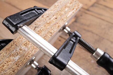 Carpentry clamp used for gluing wood. Small carpentry work in a home workshop. Light background.