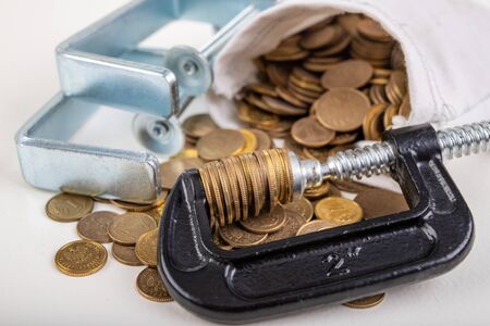 Coins squeezed in a carpenter's clamp. The image of the European currency in crisis. White background.の写真素材