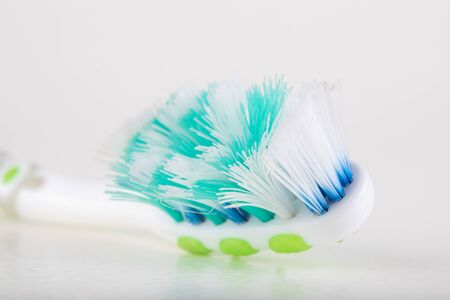 Toothbrush on a white table. Heavily worn bristles in a personal hygiene brush. Light background.