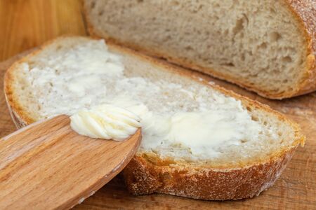 Butter spreading on fresh bread. Bread in the home kitchen. Dark background.