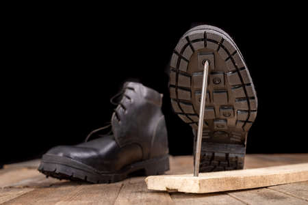 New work shoes pierced with a metal nail. Accidents at work of construction workers. Dark background.の写真素材