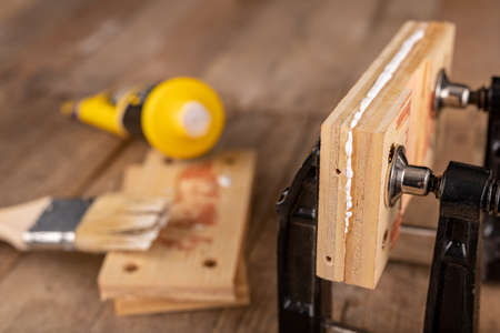 Glued wood in a carpentry clamp. Minor carpentry work in a home workshop. Light background.の写真素材