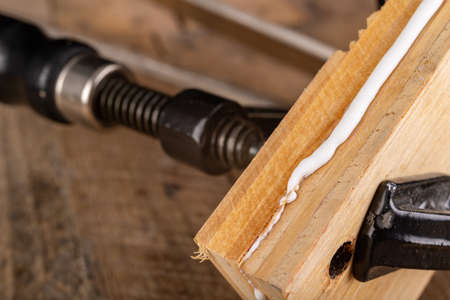 Glued wood in a carpentry clamp. Minor carpentry work in a home workshop. Light background.の写真素材