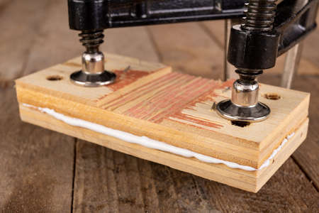 Glued wood in a carpentry clamp. Minor carpentry work in a home workshop. Light background.の写真素材