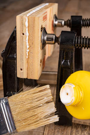 Glued wood in a carpentry clamp. Minor carpentry work in a home workshop. Light background.の写真素材