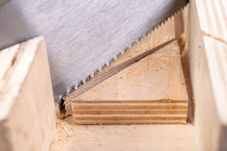 Cutting boards with a handsaw at an angle in the template. Minor carpentry work in the workshop. Light background.の写真素材