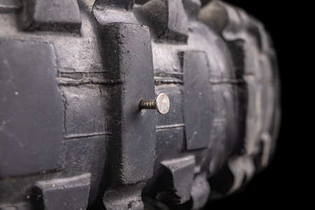 A nail in a motorcycle tire. Damaged tire with high tread. Dark background.の写真素材