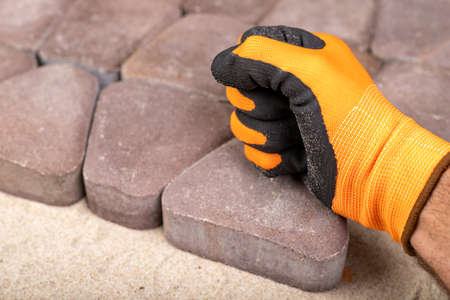 Laying paving stones on sand. Concrete cube in the hand of a builder. Light background.の写真素材