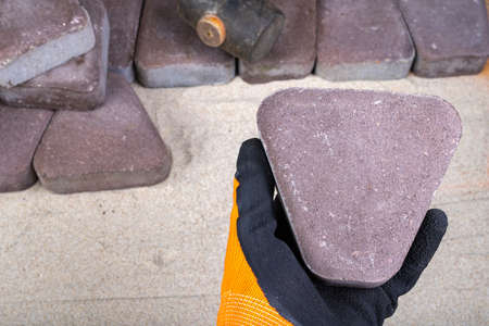 Laying paving stones on sand. Concrete cube in the hand of a builder. Light background.の写真素材