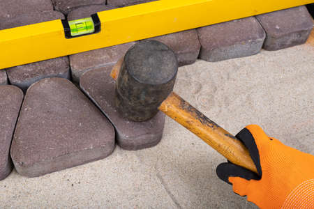 Laying paving stones on sand. Concrete cube in the hand of a builder. Light background.の写真素材