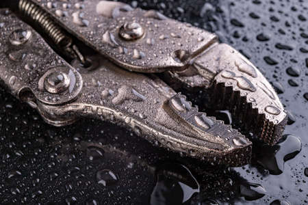Adjustable hydraulic pipe wrench covered with water. Accessories for hydraulic technicians. Dark background.の写真素材