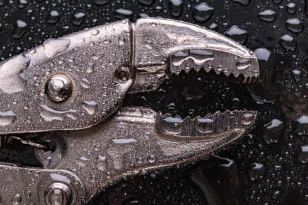 Adjustable hydraulic pipe wrench covered with water. Accessories for hydraulic technicians. Dark background.の写真素材