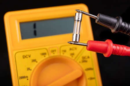 Voltmeter and glass fuse. Measurements and repairs in an electronics workshop. Dark background.の写真素材