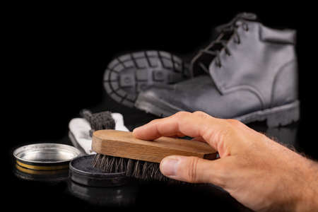 Polishing and cleaning leather shoes with a brush. Cleaning work shoes. Dark background.の写真素材