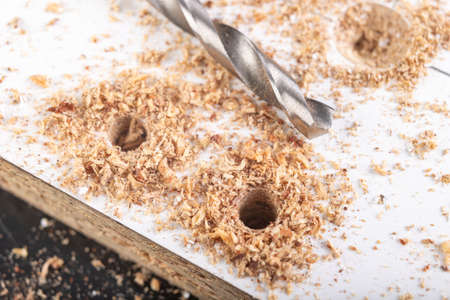Making holes with a metal drill in a chipboard. Minor jobs in the carpentry workshop. Light background.の写真素材
