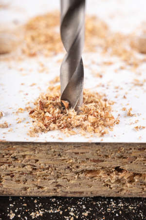 Making holes with a metal drill in a chipboard. Minor jobs in the carpentry workshop. Light background.の写真素材