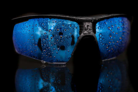 Wet bicycle glasses on a dark table. Raindrops on the surface of the sun protection goggles. Black background.の写真素材