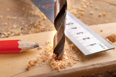 Creating holes with a metal drill in a piece of wood. Metal ruler for measuring the distance between the holes. Light background.の写真素材