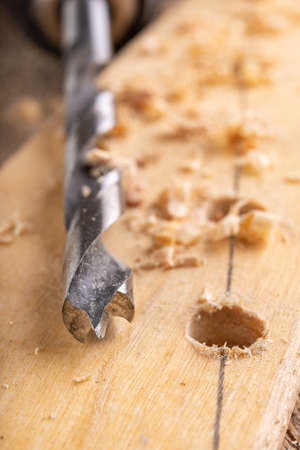 Creating holes with a metal drill in a piece of wood. Minor carpentry work in a home workshop. Light background.の写真素材