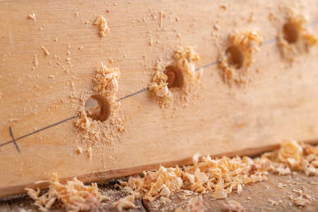 Creating holes with a metal drill in a piece of wood. Minor carpentry work in a home workshop. Light background.の写真素材