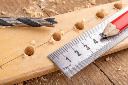 Creating holes with a metal drill in a piece of wood. Metal ruler for measuring the distance between the holes. Light background.の写真素材
