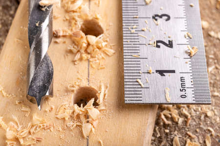 Creating holes with a metal drill in a piece of wood. Metal ruler for measuring the distance between the holes. Light background.の写真素材