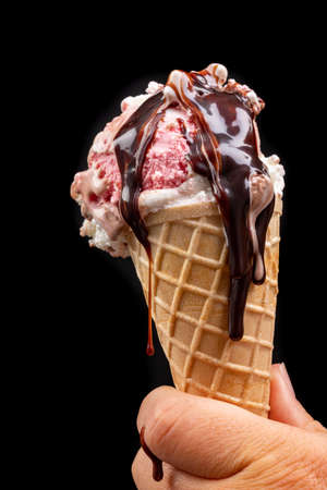 Tasty wafer ice cream in hand with chocolate glaze. Fruit dessert in a crispy wafer. Black background.の写真素材