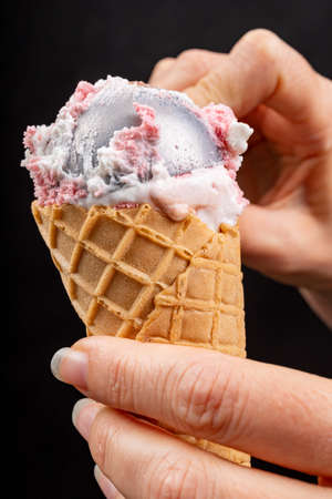 Topping on tasty ice cream with an ice cream spoon. Fruit dessert in a crispy wafer. Black background.の写真素材