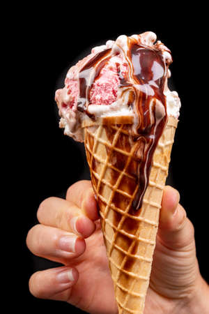 Tasty wafer ice cream in hand with chocolate glaze. Fruit dessert in a crispy wafer. Black background.の写真素材