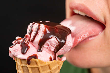 Licking tasty ice cream in a wafer held in your hand. Fruit dessert in a crispy wafer. Black background.の写真素材
