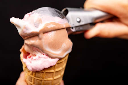 Topping on tasty ice cream with an ice cream spoon. Fruit dessert in a crispy wafer. Black background.の写真素材