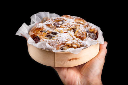 Tasty fruit cake in a paper mold held in the palm of your hand. Dessert prepared for serving. Dark background.の写真素材