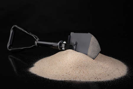 Black military shovel in the sand. Military accessories for excavating anti-personnel mines. Dark background.の写真素材
