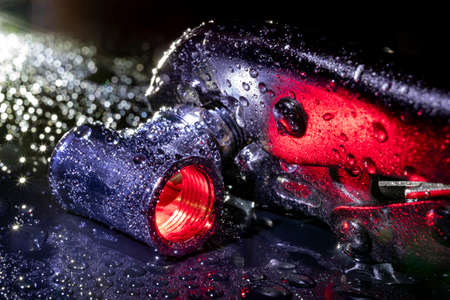 Clamp wrench with a metal tube covered with water. Plumbing accessories in bright light. Dark background.の写真素材