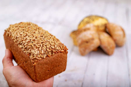 Dark bread with grains on the hand. Fresh bread in the bakery. Light background.の写真素材