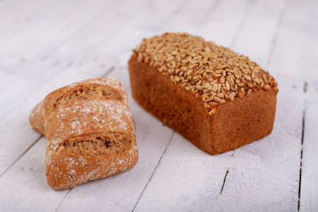 Tasty dark bread with sunflower seeds and rolls on a wooden table. Fresh bread in the bakery. Light background.の写真素材