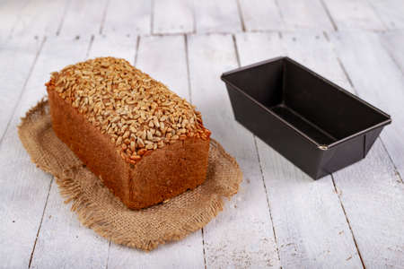 Tasty dark bread with sunflower seeds and metal molds on a wooden table. Fresh bread in the bakery. Light background.の写真素材