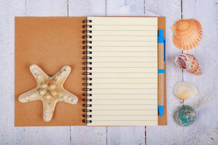Notebook for writing your vacation memories. A blank sheet and seashells from the seaside. Light background.の写真素材