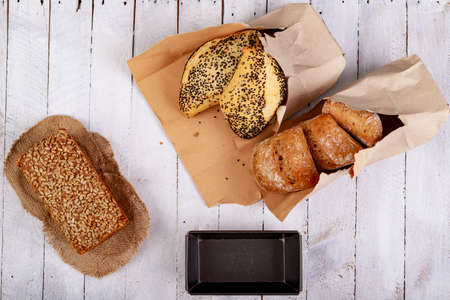 Tasty dark bread with sunflower seeds and rolls on a wooden table. Fresh bread and metal molds in the bakery.Light background.の写真素材