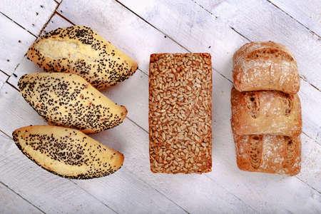 Tasty dark bread with sunflower seeds and rolls on a wooden table. Fresh bread in the bakery. Light background.の写真素材